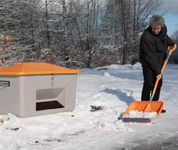 Mann räumt Schnee mit CEMO GFK Schneeschaufel. Im Hintergrund steht ein Streugutbehälter von CEMO.